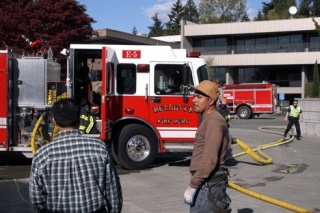 Roof workers of an unknown roofing company look on as fire units from Kirkland