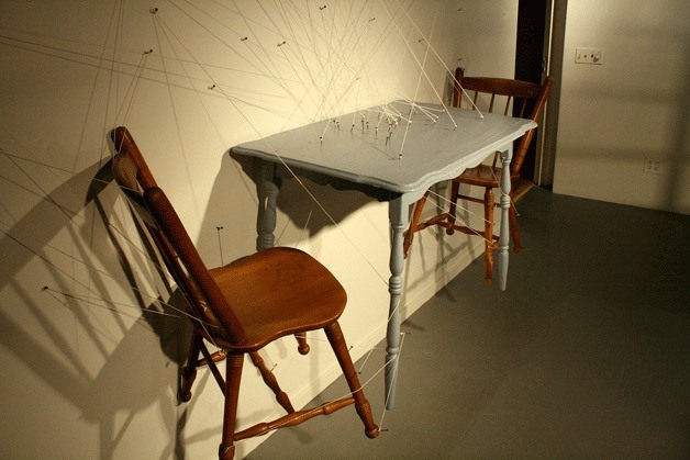 Sean M. Johnson’s “Tension at the Dinner Table” consists of heavy wood furniture supported by a complex system of strings held taut by nails. The sheer tension of strings and placement of nails provide a sense of stress to the conversation happening within these two interactions. The artwork is part of a new exhibit at the Kirkland Arts Center that opened this week.