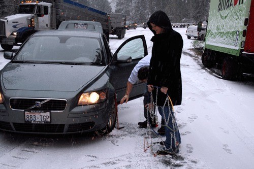 Elevation was everything Monday morning as many Kirkland streets were clear but the tops of local hills were not. Rachel Severinsen holds a set of car chains and Jordan Kamal finishes putting a set on the front tire in the middle of Juanita Drive N.E. on Finn Hill. An accident caused a blockage on the road and many had to turn around or chain up.