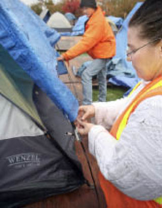 Debra and Jack Exum work to secure a tarp over their tent to keep the rain out at Tent City 4