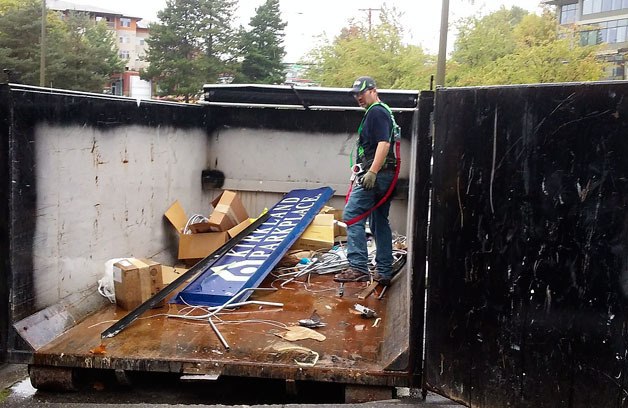 A worker stands in a garbage dumpster along with one of the Parkplace signs that used to adorn the brick building in downtown Kirkland.
