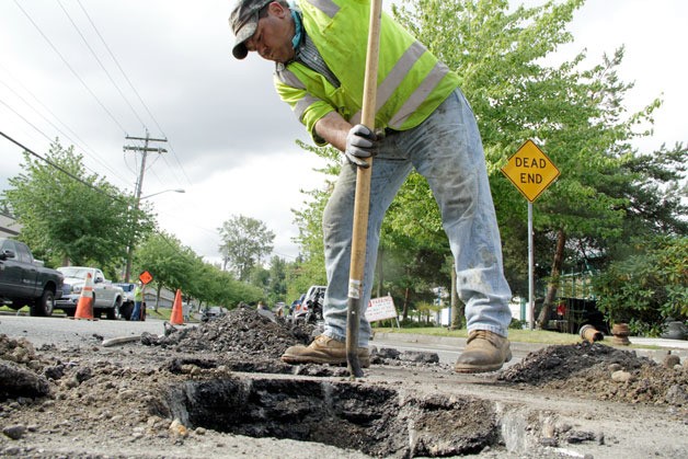 Watson Asphalt laborer T Pelayo digs around a water main utility Monday on 120th Avenue Northeast as part of the lowering iron process