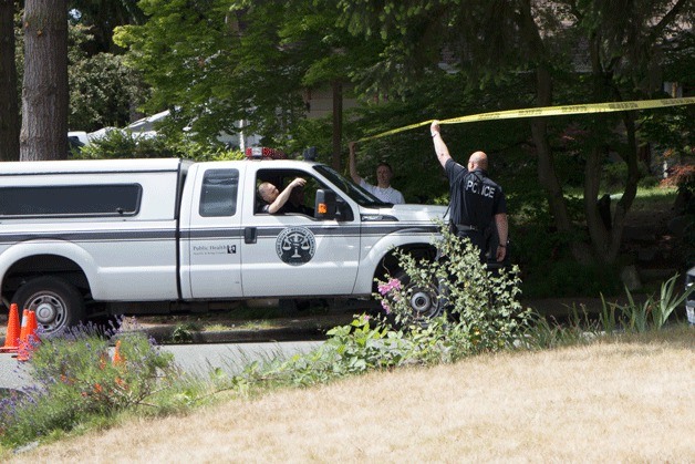 A police officer raises yellow crime tape to allow the King County Coroner's vehicle onto a street where a fatal house fire took place on Wednesday evening.