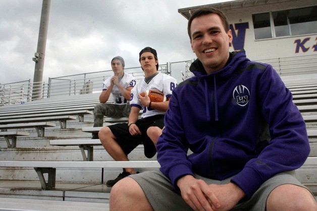New Lake Washington High School football coach AJ Parnell sits in the Mac Field stands with football players Braun Inslee