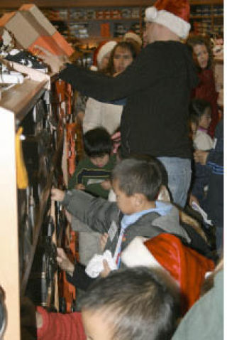 Top left: Volunteer Karen Tabler (wearing Santa hat) and brothers Mike (red coat) and Justin Chong (not pictured) try to find a pair of shoes. Top right: Totem Lake Fred Meyer Store Manager Kevin Elicker opens the doors to the first of 300 kids and their families. Bottom left: Cristian Morelos