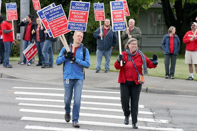 Juanita High School teachers Toby Welch and Kim Roberts hold up signs at the intersection of Northeast 132nd Street and 100th Avenue Northeast near Juanita Elementary during a walkout on Wednesday to protest the state legislature not complying with the State Supreme Court’s decision concerning funding for K-12 education.