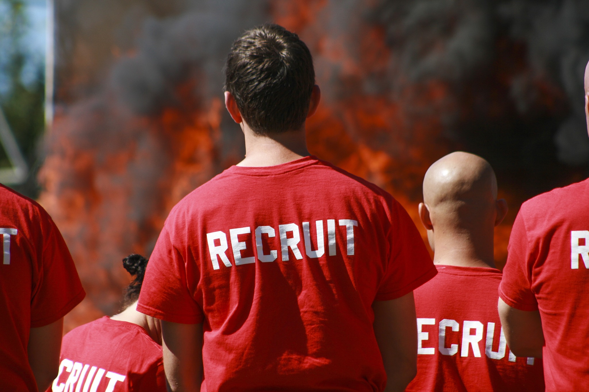 Recruits stand in front of a controlled burn behind the North Rose Hill fire station on Monday
