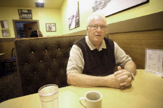 Bill Woods glances over at the TV while having coffee (and chatting with a reporter) at George’s Place on July 3.