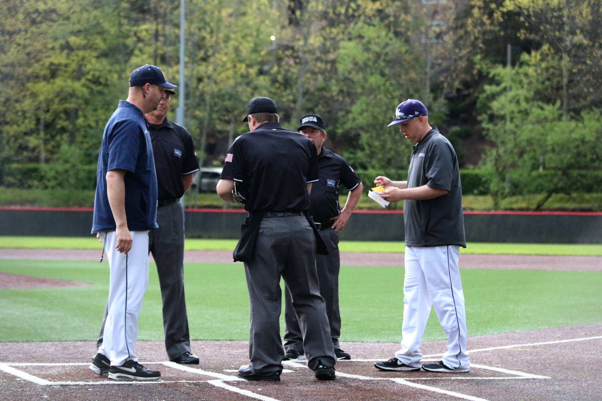 Lake Washington and Bellevue coaches and umpires gather at home plate this evening at Bannerwood Park. At this point, the game was to start an hour late at about 5 p.m. because of lightning, but was postponed for the evening a few minutes later when more lightning appeared. Andy Nystrom, Kirkland Reporter