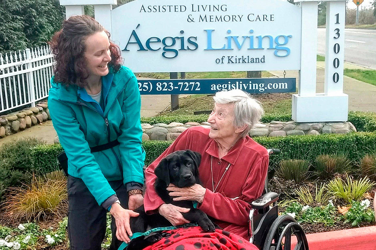 Lindy Langum, the Summit Assistance Dog trainer, helps a senior from Aegis Living hold one of the puppies-in-training. Courtesy of Aegis Living.