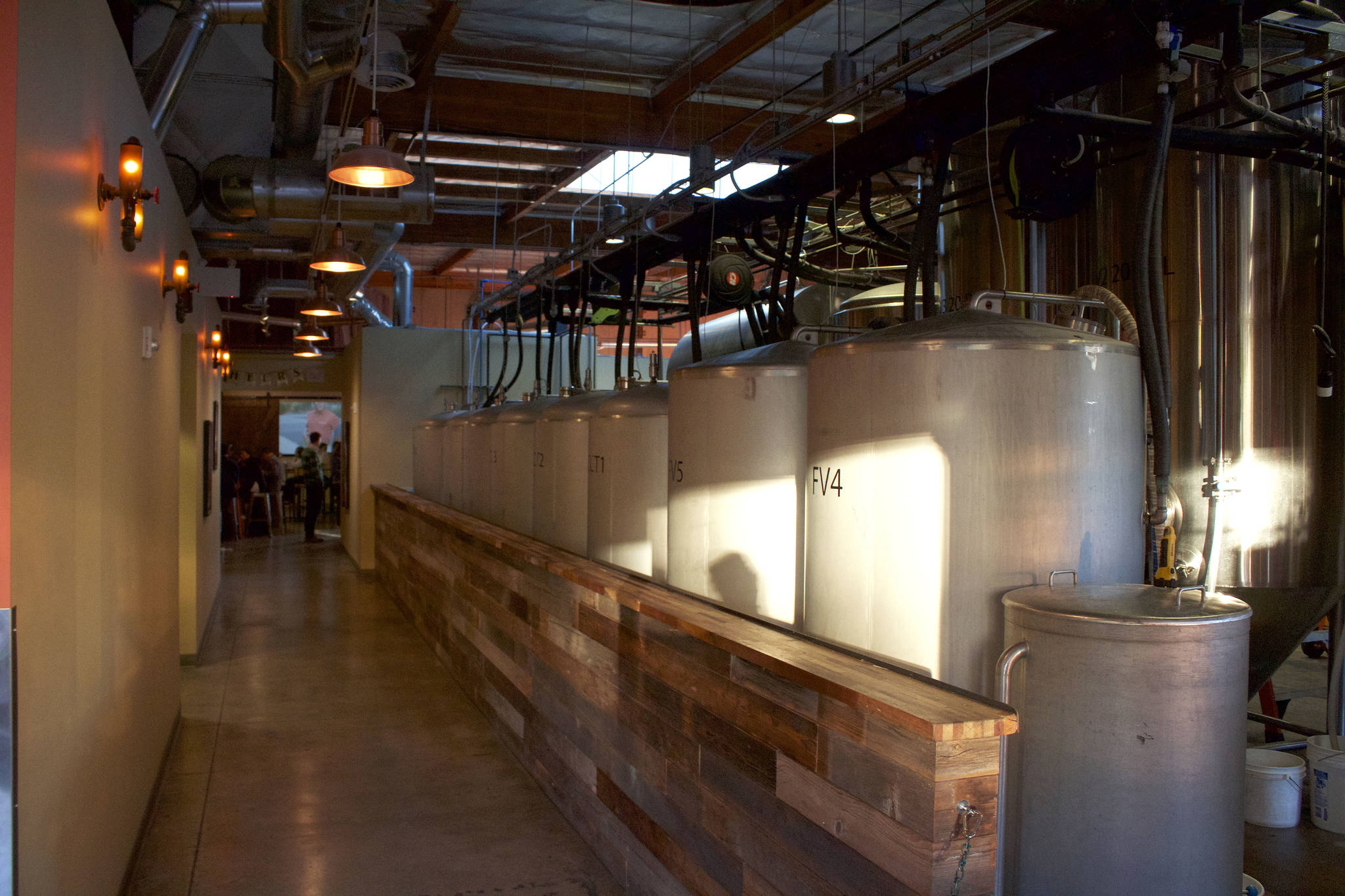 Chainline patrons walk down a line of tanks and brewing equipment before they enter the tap room at the back of the space. Kailan Manandic/staff photo