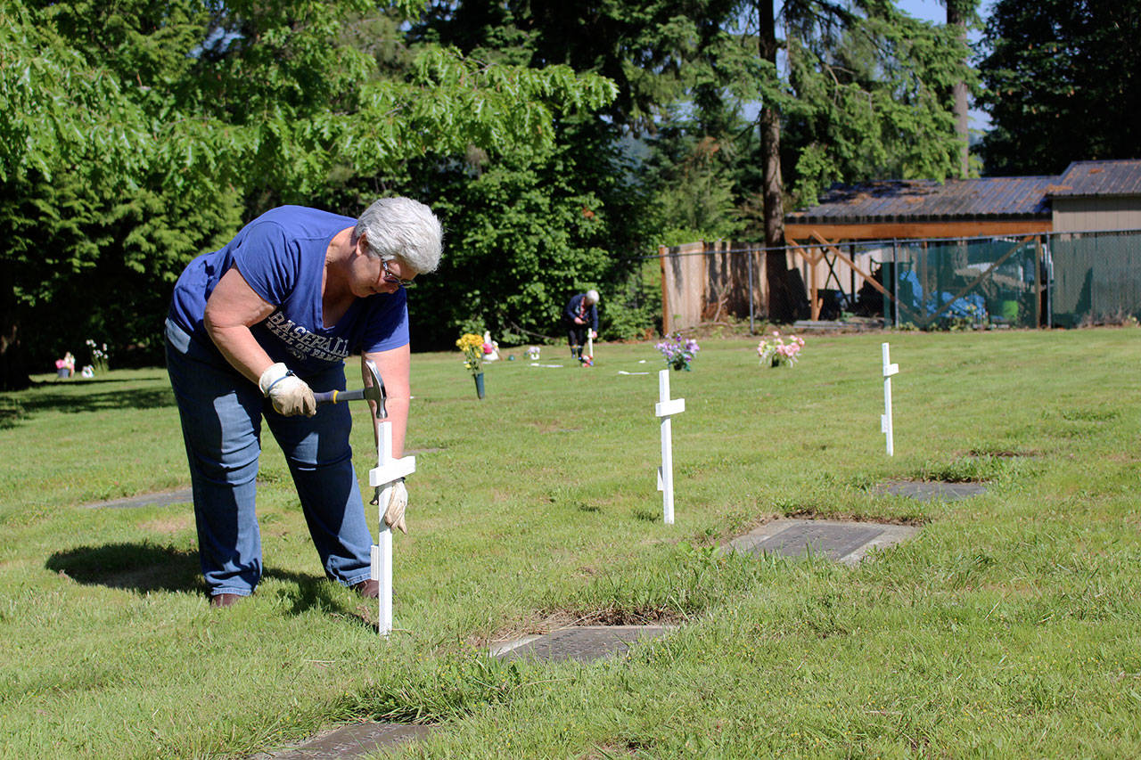 Community volunteer Bonnie Mcleod hammers a white cross into the ground above a local veterans grave to commemorate their service. Kailan Manandic / staff photo