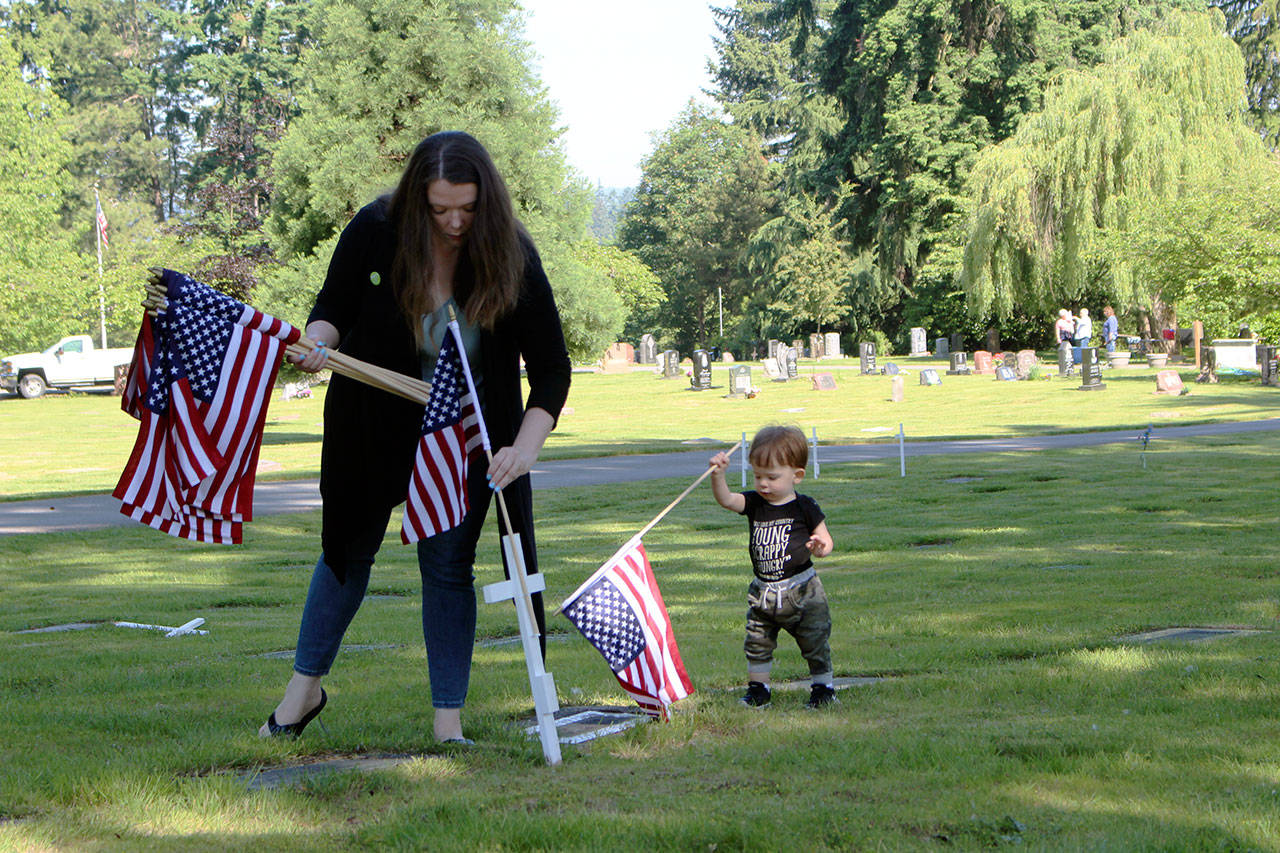 Kirkland City Council candidate Amy Falcone and her one-year-old son Rocky honor local veterans by planting U.S. flags among the white crosses commemorating their graves. Kailan Manandic / staff photo