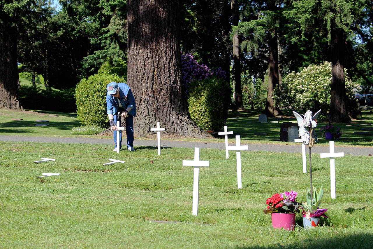 Community volunteer Janis Lucas hammers a white cross into the ground above a local veterans grave to commemorate their service. Kailan Manandic / staff photo