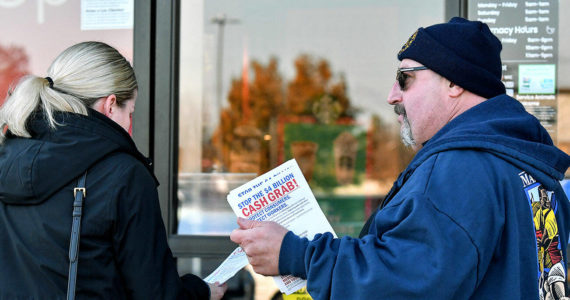 Kevin Flynn, right, a meat-cutter with the Marysville Albertsons, hands a leaflet to a shopper during an informational campaign on Wednesday, Nov. 9, 2022. Flynn was one of about a dozen grocery store workers handing out leaflets to shoppers about the proposed merger between Albertsons and Kroger. (Mike Henneke / The Herald)