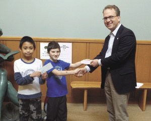 Red Cross Representative Steven Greimann accepts checks from Thoreau students Zeke Marsh and Fraxz Padilla.