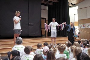 Betsy Hills speaks to students as the St. Thomas School Director Kirk Wheeler stands draped in her medals that were stolen on Dec. 2.