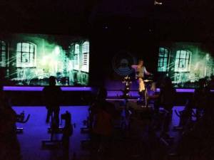 Bassline Fitness owner Dave Fox encourages class members to work to the beat of the music video on the screen during a recent class.